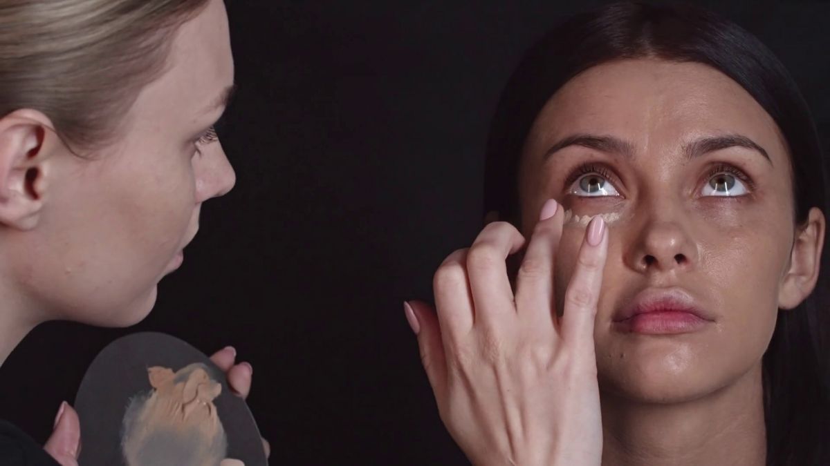 closeup-of-professional-makeup-artist-applying-concealer-under-eyes-of-young-woman-with-fingers-and-then-using-brush-to-blend-it_rjg7zaldp_thumbnail-full01